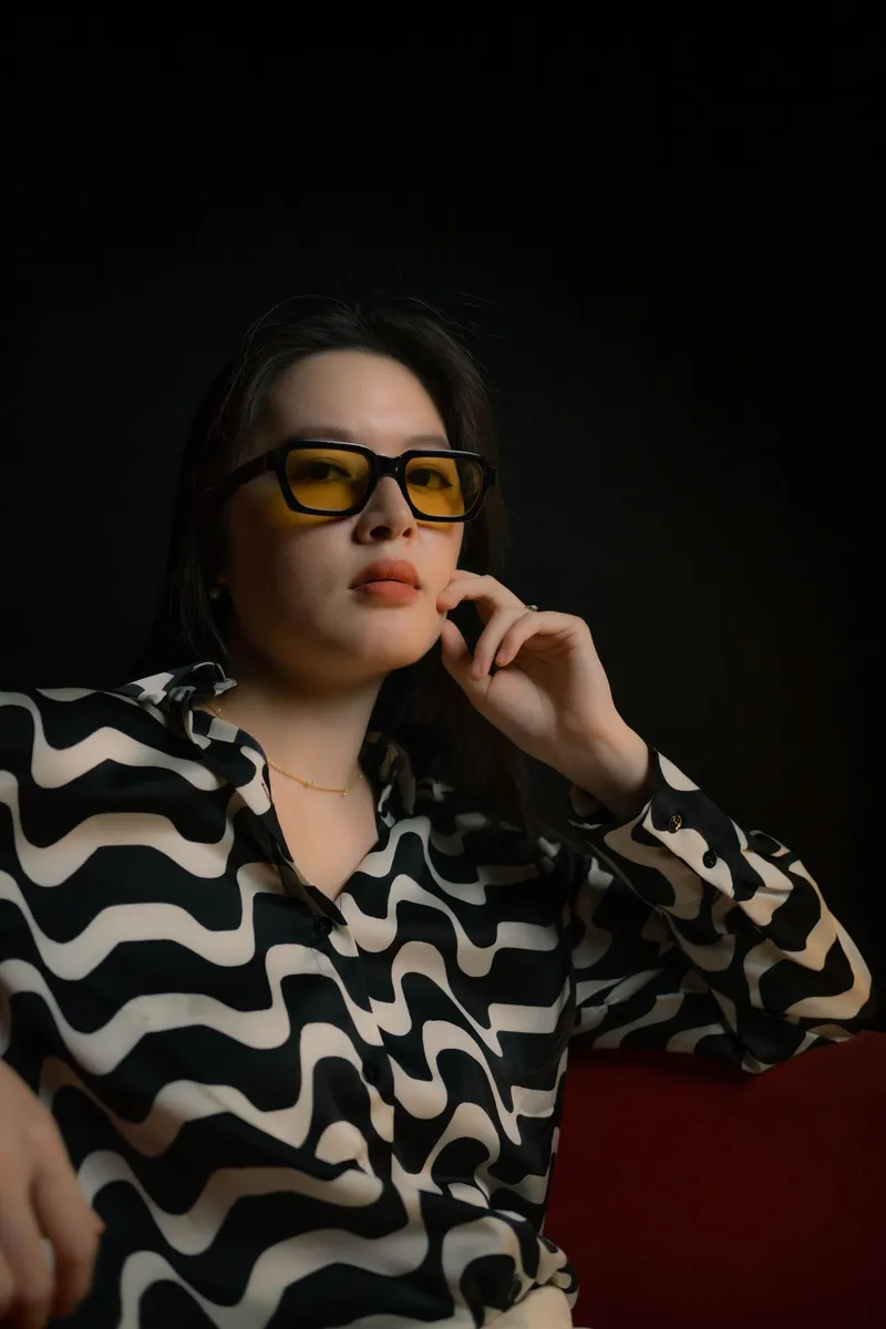 Una mujer con camisa estampada y gafas de lente amarilla sobre fondo negro