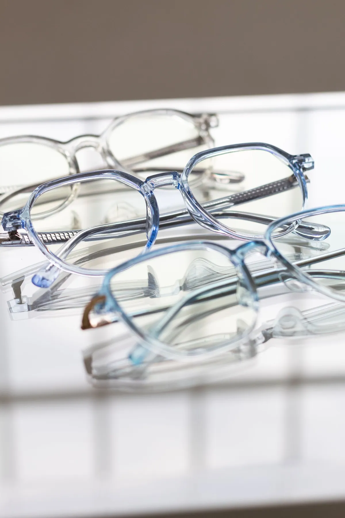 Varias monturas de gafas translúcidas y azuladas sobre una superficie reflectante