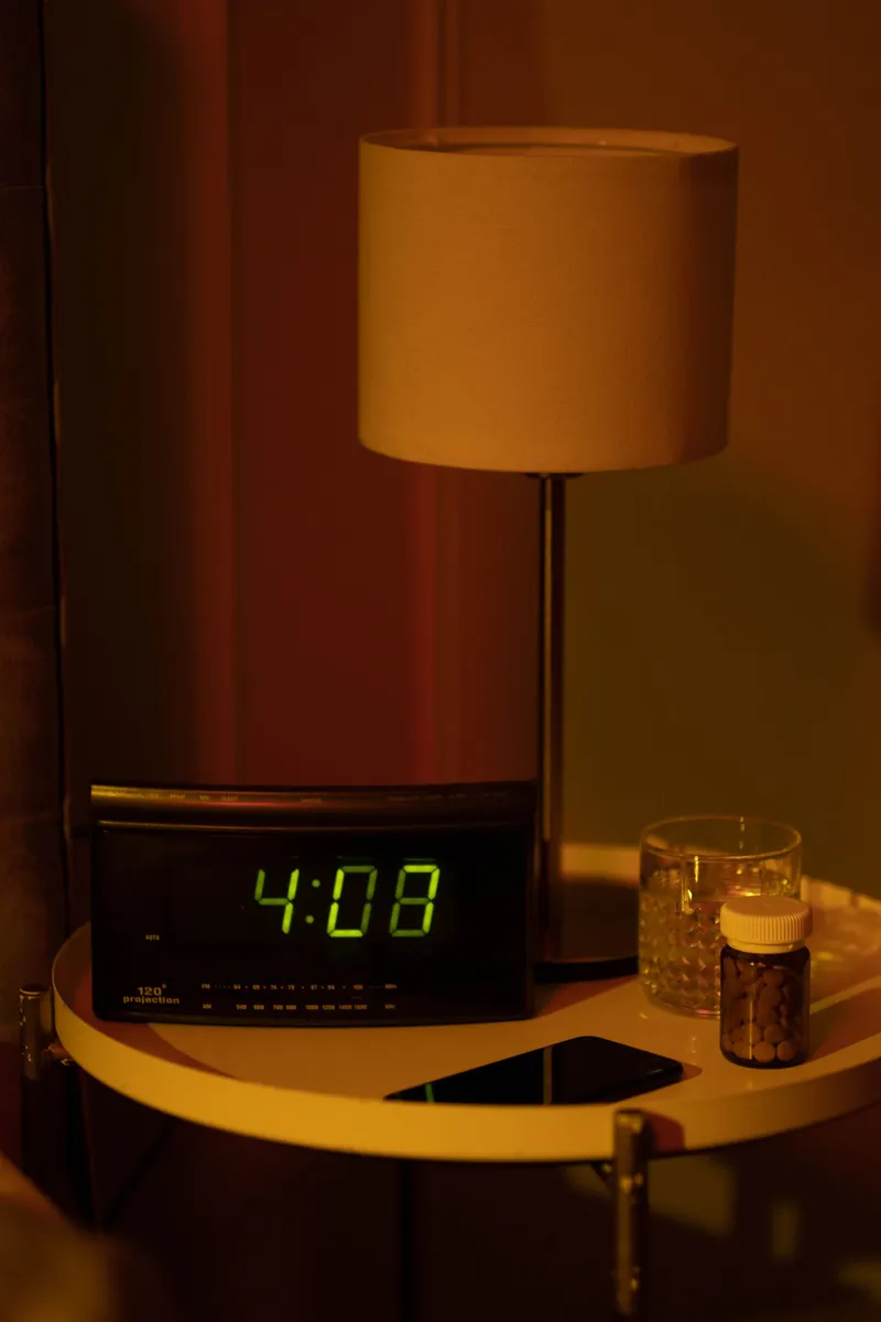 Un despertador digital y una pastilla sobre la mesilla de noche con luz tenue
