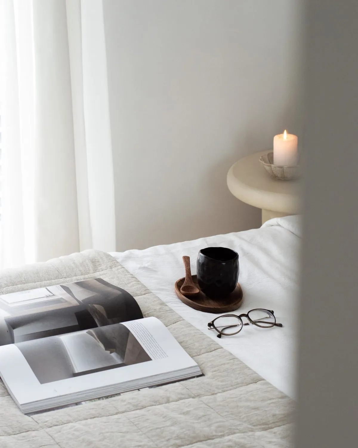 Escena minimalista de mesilla de noche con gafas, un libro y la luz de una vela