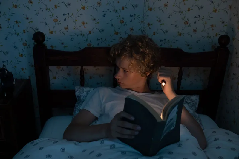 Adolescente leyendo un libro en la cama por la noche antes de dormir