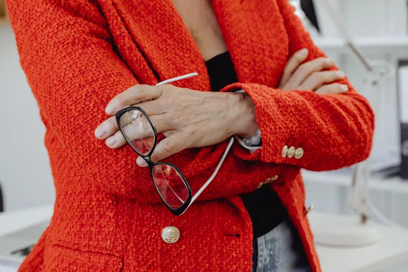 Una mujer con blazer rojo sosteniendo unas gafas en la mano
