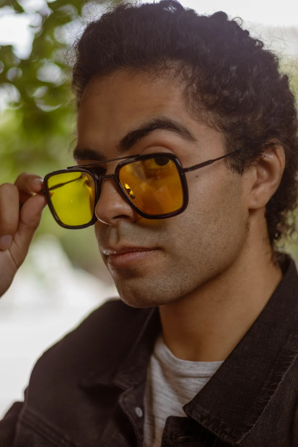 Un joven con el pelo rizado luciendo gafas de sol de lente amarilla al aire libre