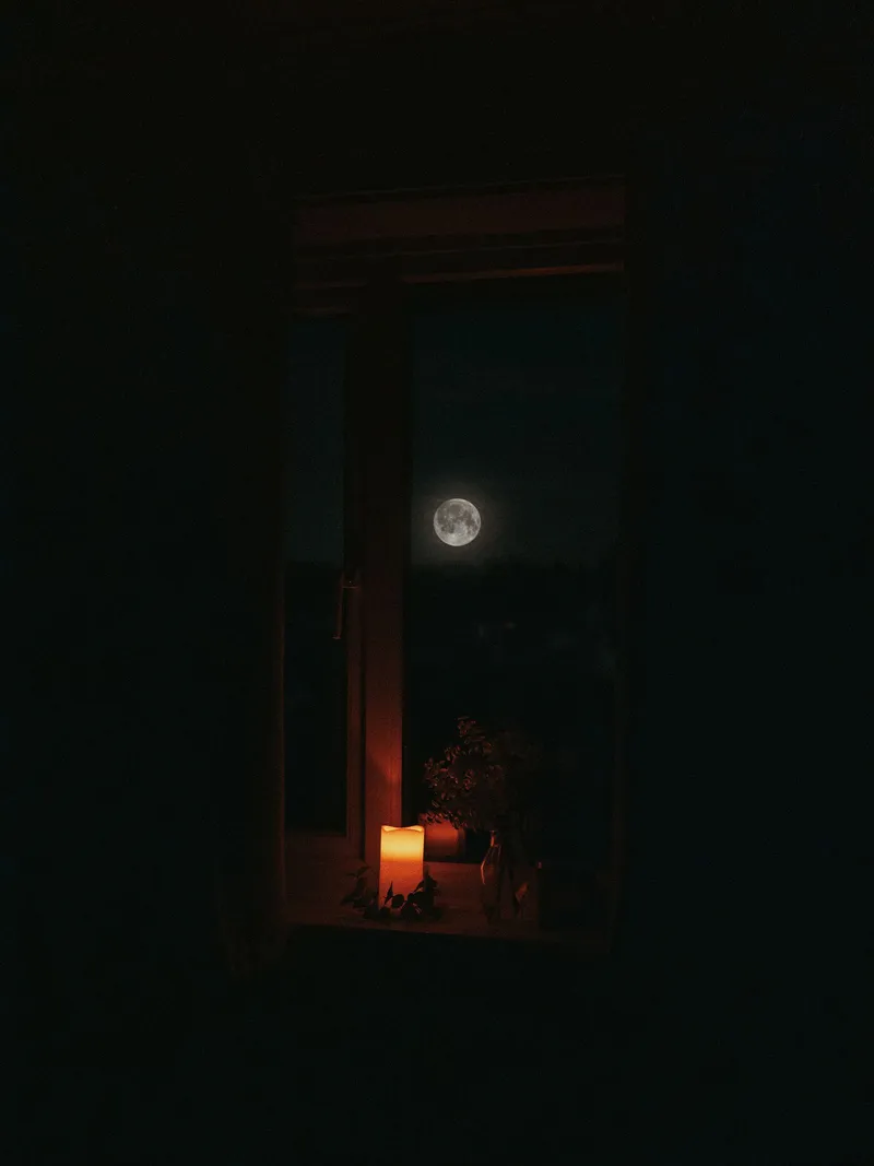 La luna vista a través de una ventana con el suave resplandor de una vela