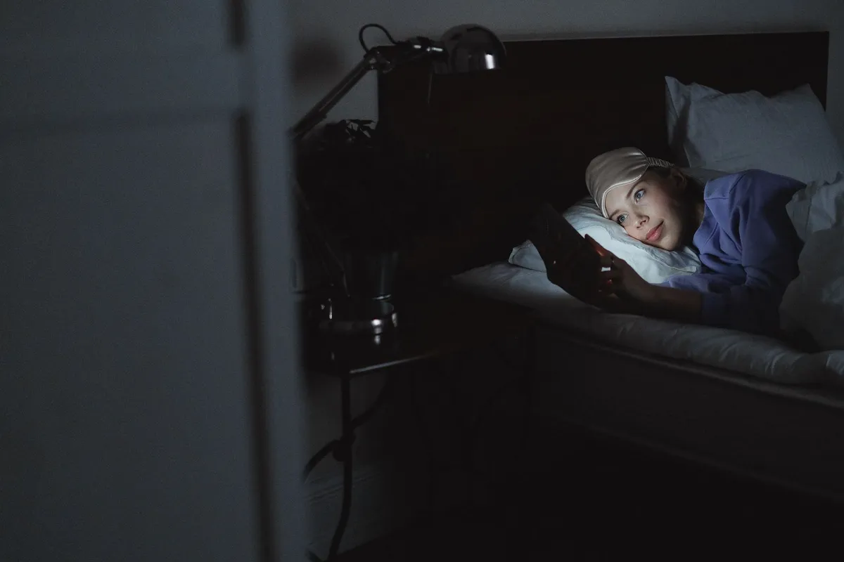 Una mujer en la cama de noche con el rostro iluminado por la pantalla del móvil