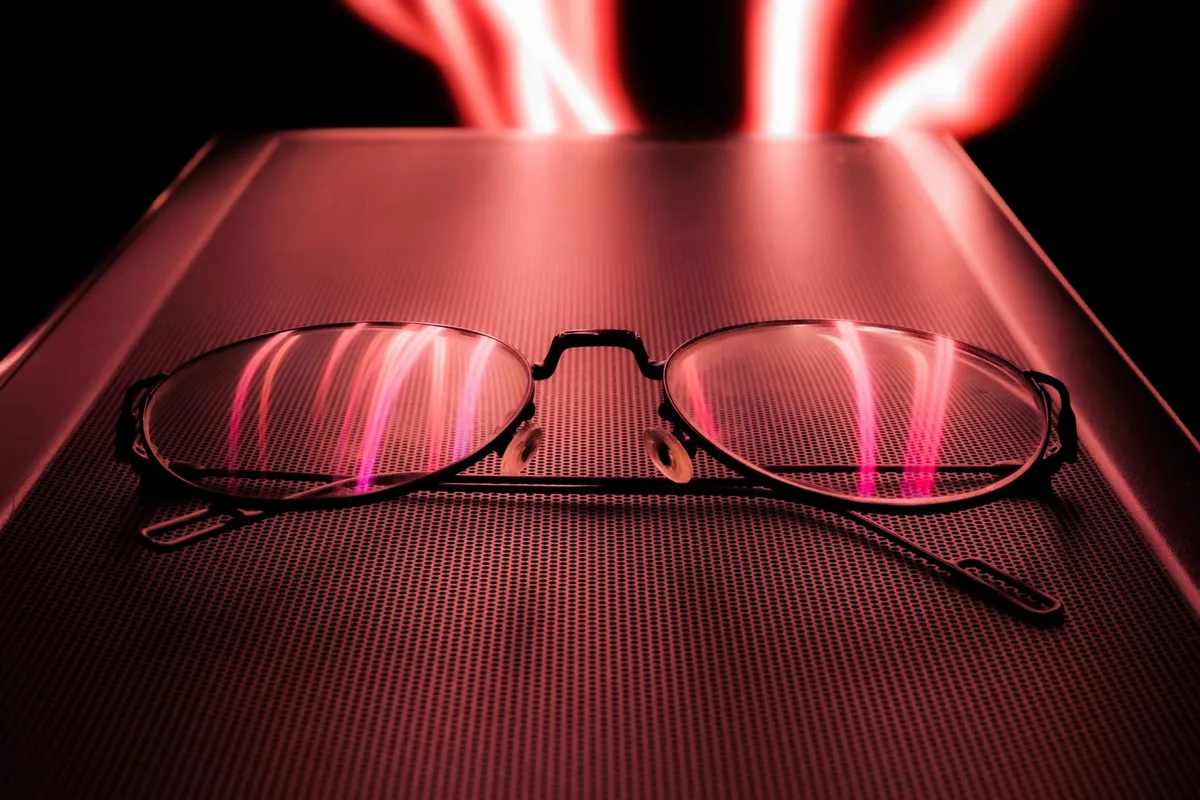 Unas gafas reflejando estelas de luz roja sobre una superficie oscura